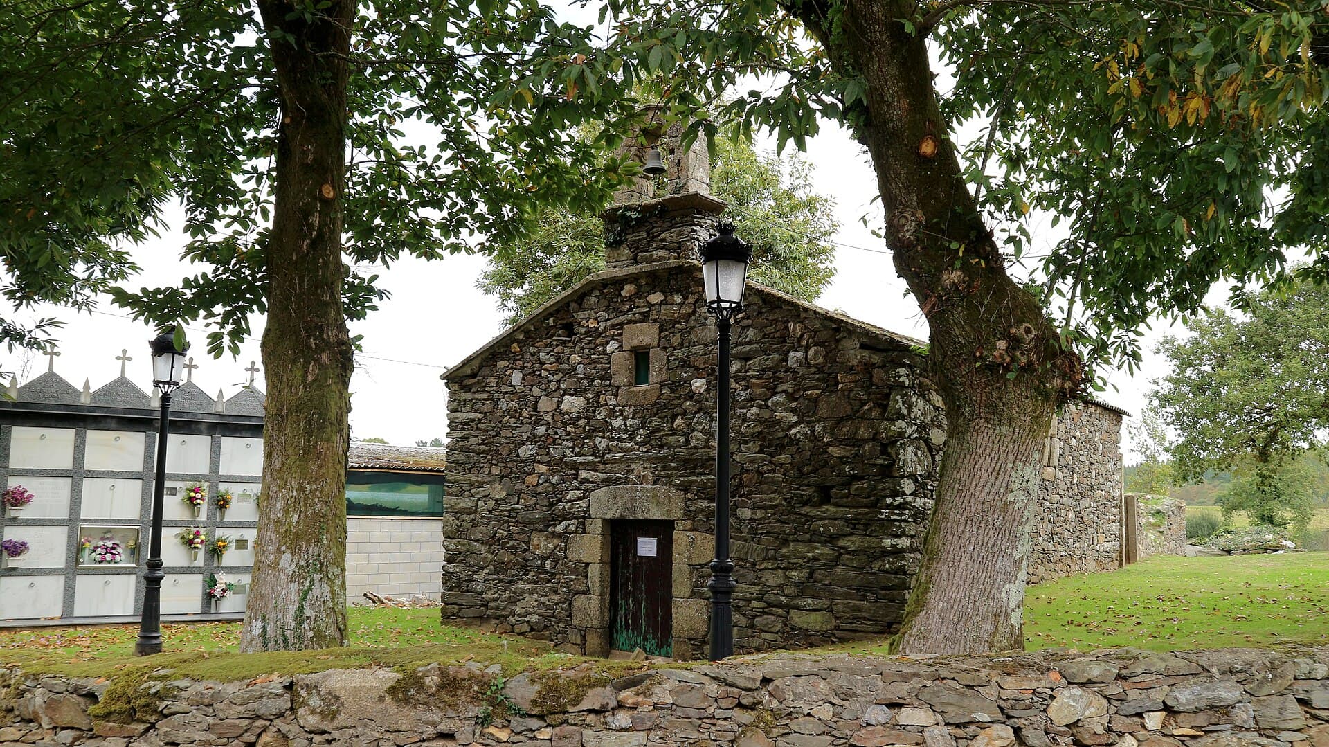 Small granite parish church of San Lourenzo at Hospital de Bruma, between two trees.